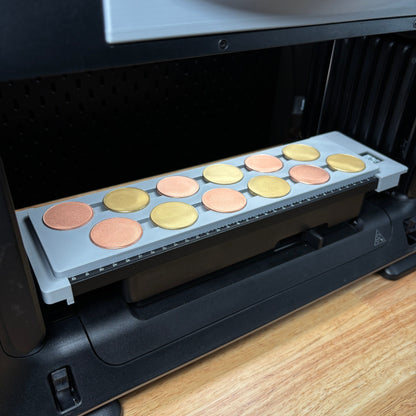 Samcraft 40mm metal coin jig on the eufyMake E1 print bed, holding a row of gold and silver metal coin blanks.
