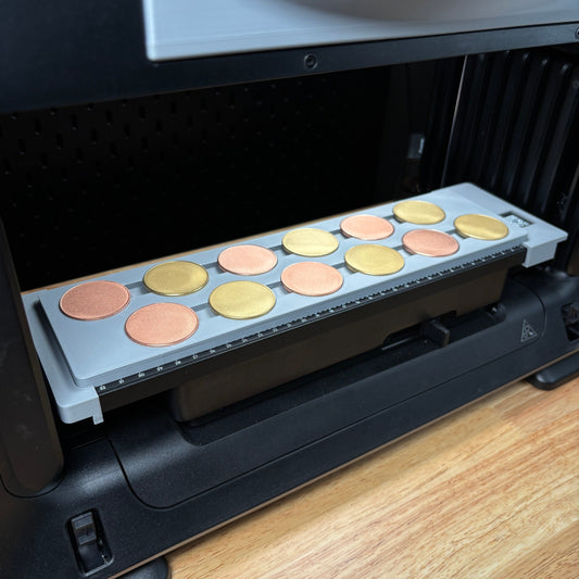 Samcraft 40mm metal coin jig on the eufyMake E1 print bed, holding a row of gold and silver metal coin blanks.