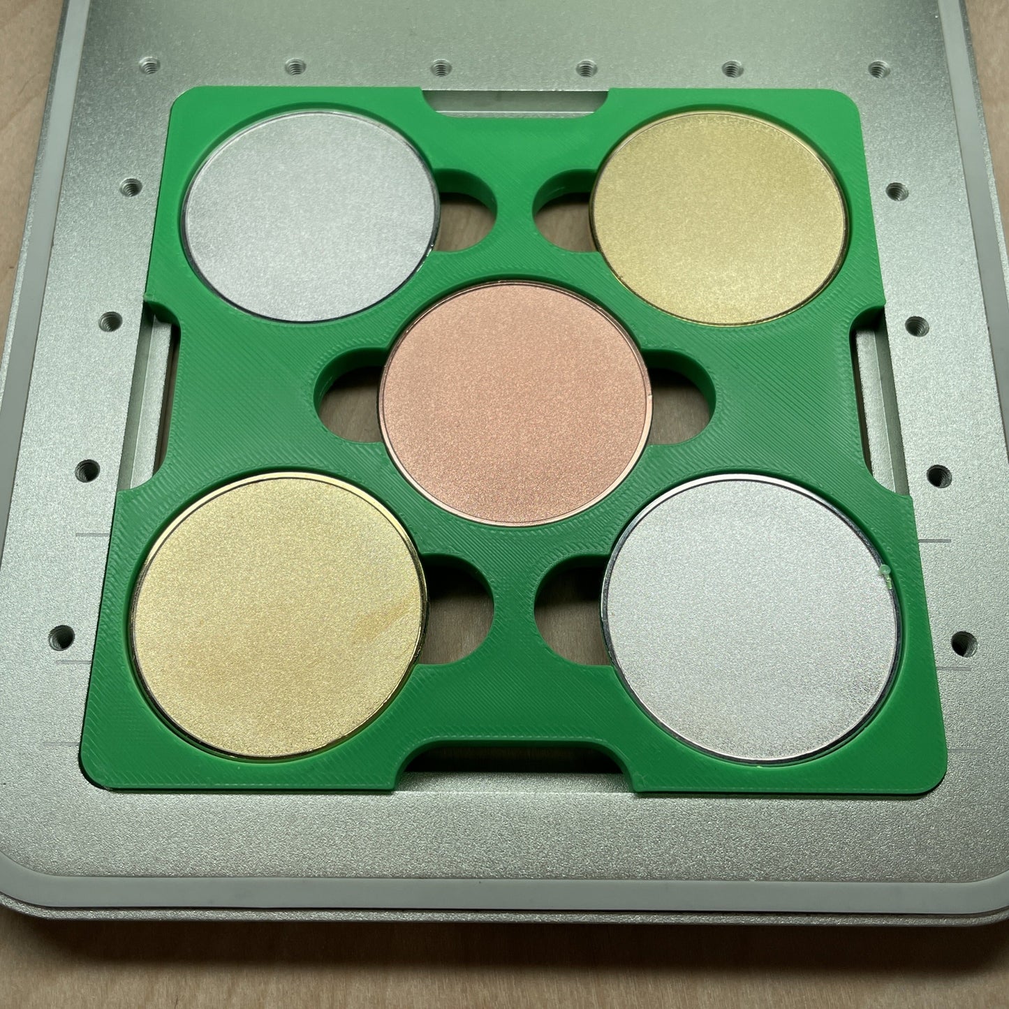 Samcraft green 40mm metal coin jig in an xTool F1 laser bed, holding gold, silver and copper coin blanks.