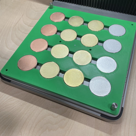 Samcraft green metal coin jig in an xTool F1 Ultra laser bed, holding a full grid of gold, silver, copper and rose coin blanks.