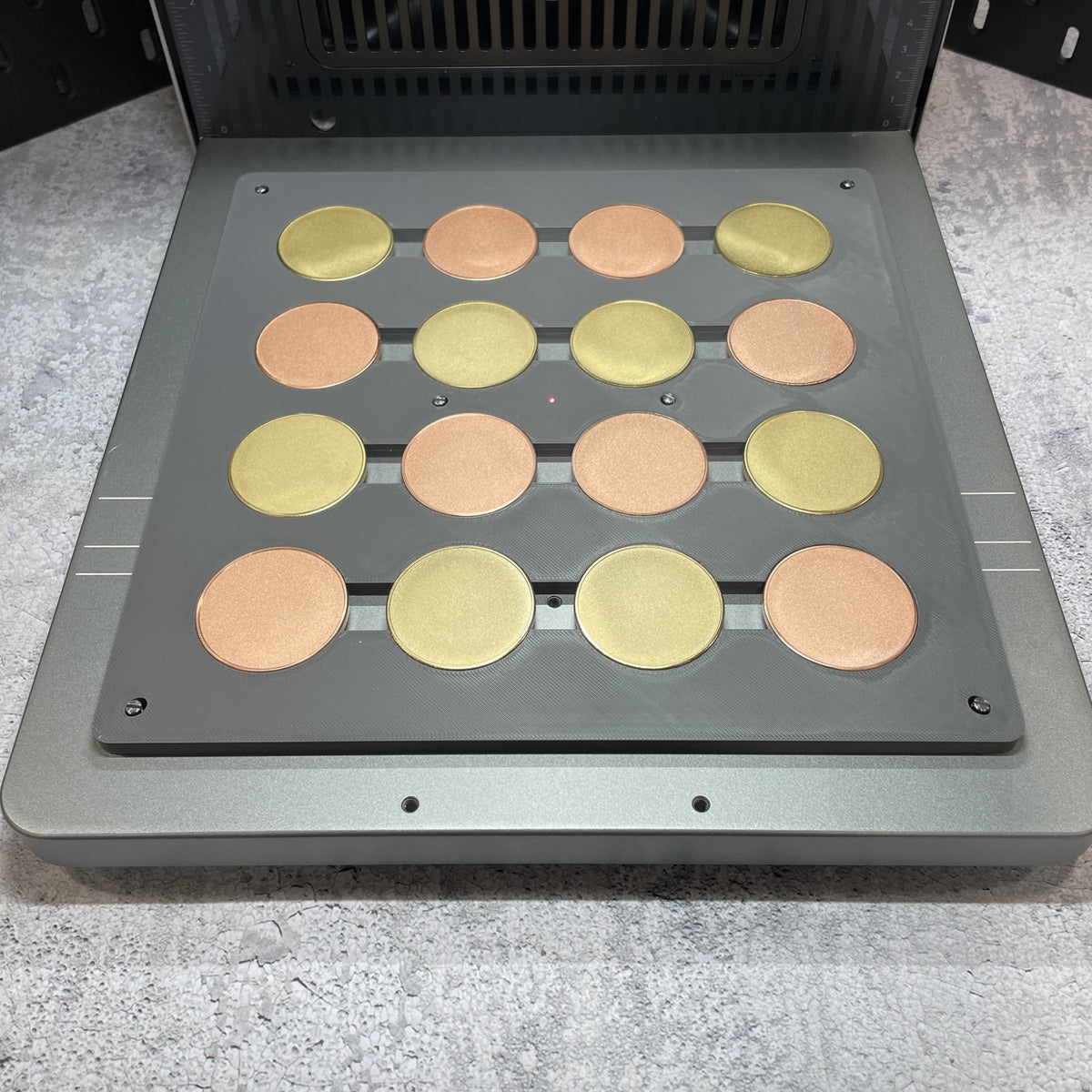 Samcraft grey metal coin jig on the xTool F2 Ultra bed, holding a full grid of gold and copper coin blanks.