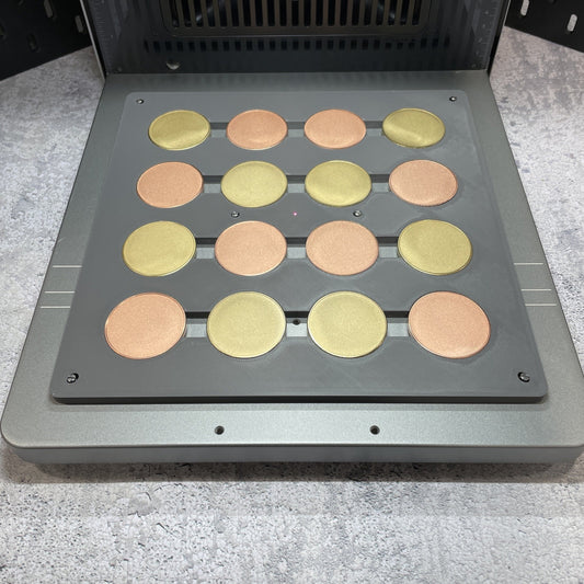 Samcraft grey metal coin jig on the xTool F2 Ultra bed, holding a full grid of gold and copper coin blanks.