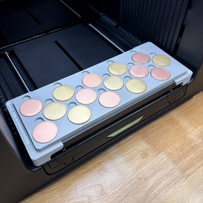 Samcraft 40mm metal coin jig on the bed of an xTool Omni UV printer, holding fifteen rose gold and gold blank challenge coins, seated on the Omni Jig Alignment System.