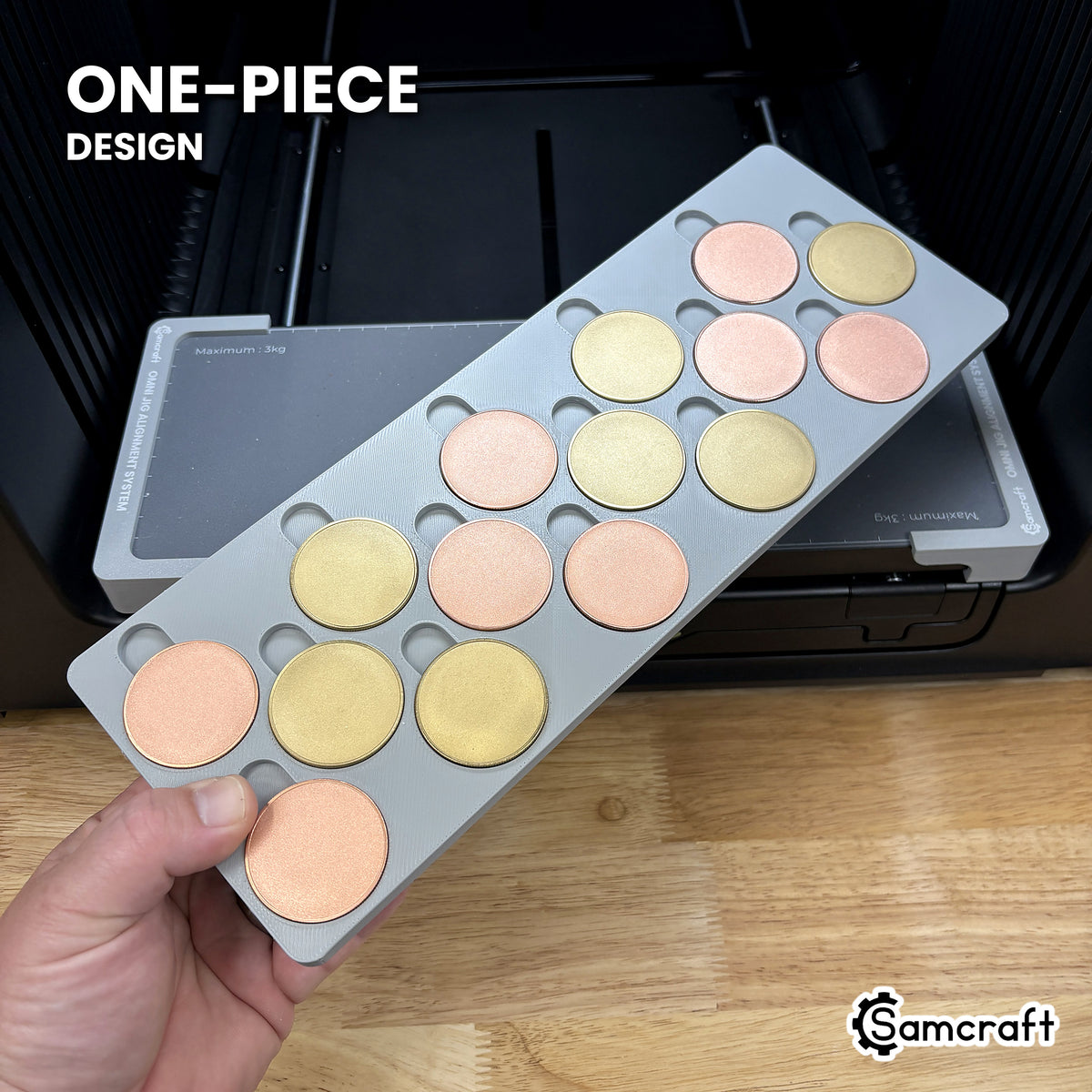 Hand holding the one-piece Samcraft 40mm metal coin jig for the xTool Omni, fifteen blank coins seated in a single molded gray tray.