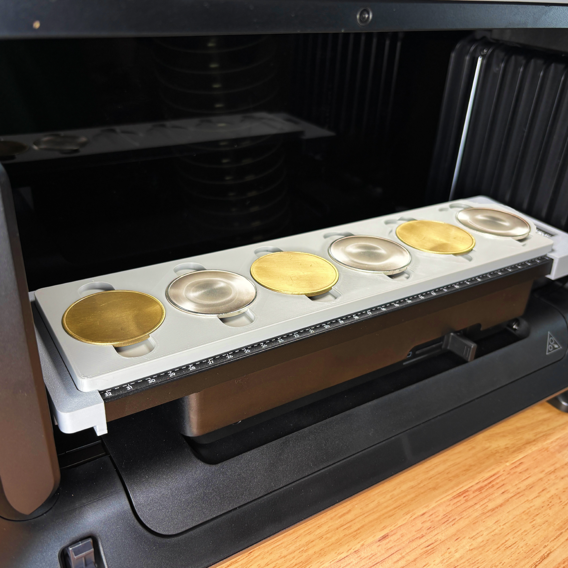 Samcraft 50mm metal coin jig on the eufyMake E1 print bed, holding six alternating gold and silver metal coin blanks in a row.