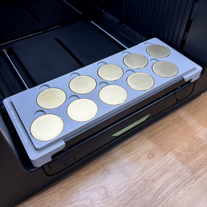 Samcraft 50mm metal coin jig on the bed of an xTool Omni UV printer, holding ten gold blank challenge coins, seated on the Omni Jig Alignment System.