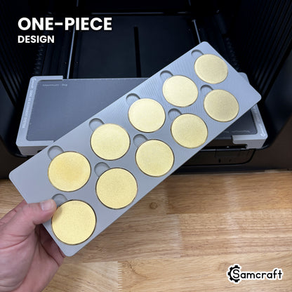 Hand holding the one-piece Samcraft 50mm metal coin jig for the xTool Omni, ten blank gold coins seated in a single molded gray tray.
