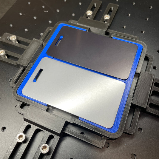 Samcraft blue metal luggage tag jig on a ComMarker laser bed, holding a silver metal luggage tag.