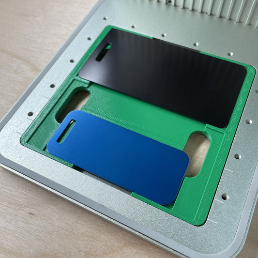 Samcraft metal luggage tag jig in an xTool F1 laser bed, holding one black and one blue aluminium luggage tag.