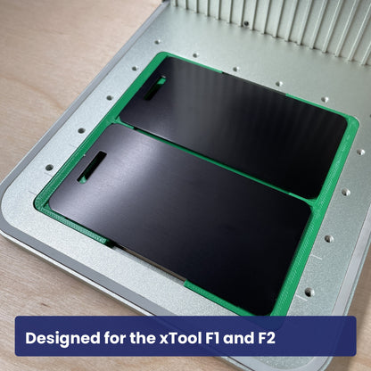 Green Samcraft luggage tag jig seated in the xTool F1 base plate, holding two black luggage tags.