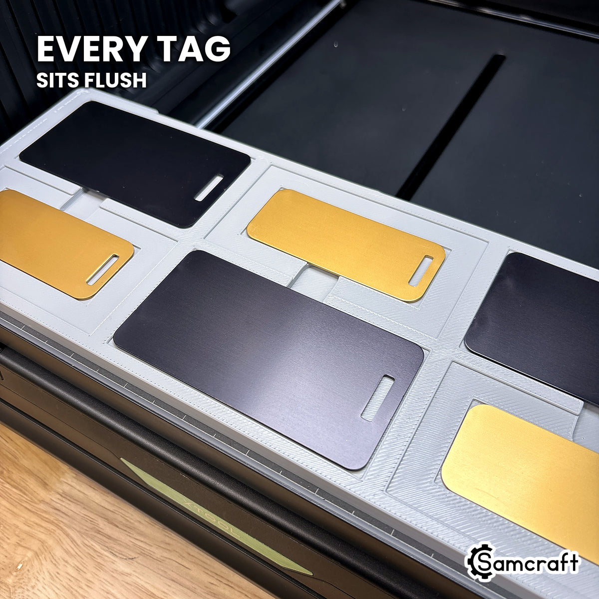 Metal luggage tag seated flush in the Samcraft xTool Omni jig pocket, level with the surrounding surface.