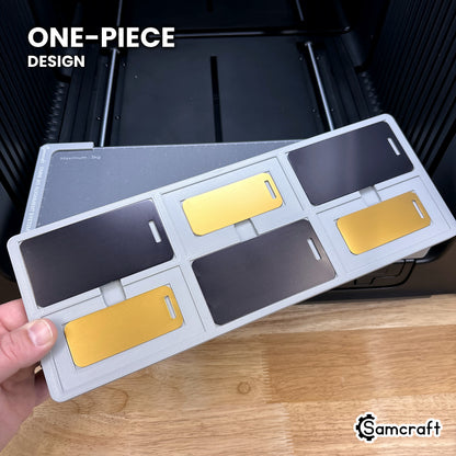 Hand holding the one-piece Samcraft metal luggage tag jig for the xTool Omni, six tag pockets in a single molded tray.