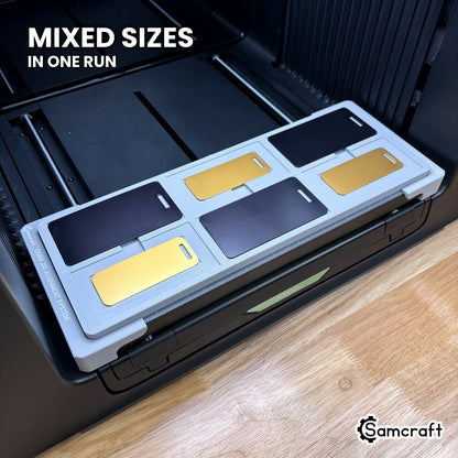 Large and small metal luggage tags loaded together in the Samcraft xTool Omni jig, both sizes printed in the same run.