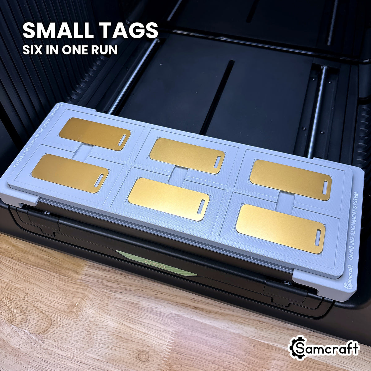Six small gold metal luggage tags seated in the inner recesses of the Samcraft xTool Omni jig, six in one run.