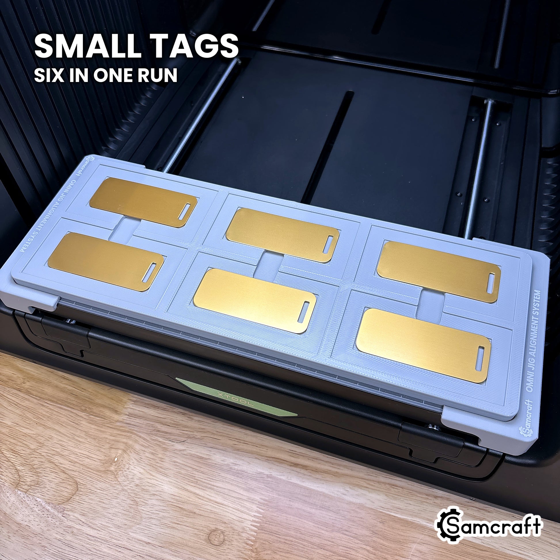 Six small gold metal luggage tags seated in the inner recesses of the Samcraft xTool Omni jig, six in one run.