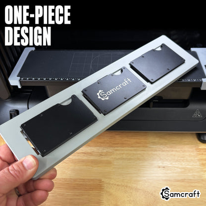 One-piece Samcraft Metal Wallet Jig held in hand above the eufyMake E1 print bed, loaded with three metal wallets