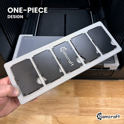Hand holding the one-piece Samcraft metal wallet jig for the xTool Omni, five wallets seated in a single molded tray.