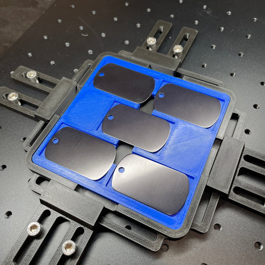 Samcraft blue military dog tag jig on a ComMarker laser bed, holding black and stainless dog tags.