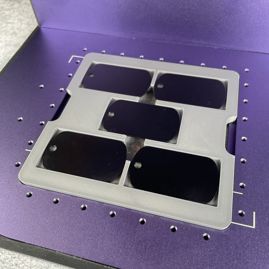 Samcraft military dog tag jig on the purple bed of a WeCreat Lumos, holding black dog tags.