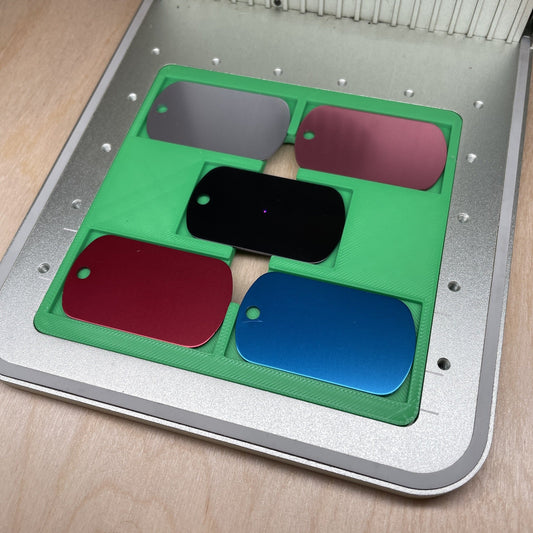 Samcraft military dog tag jig in an xTool F1 laser bed, holding five anodised aluminium dog tags in a four-corner and centre layout.