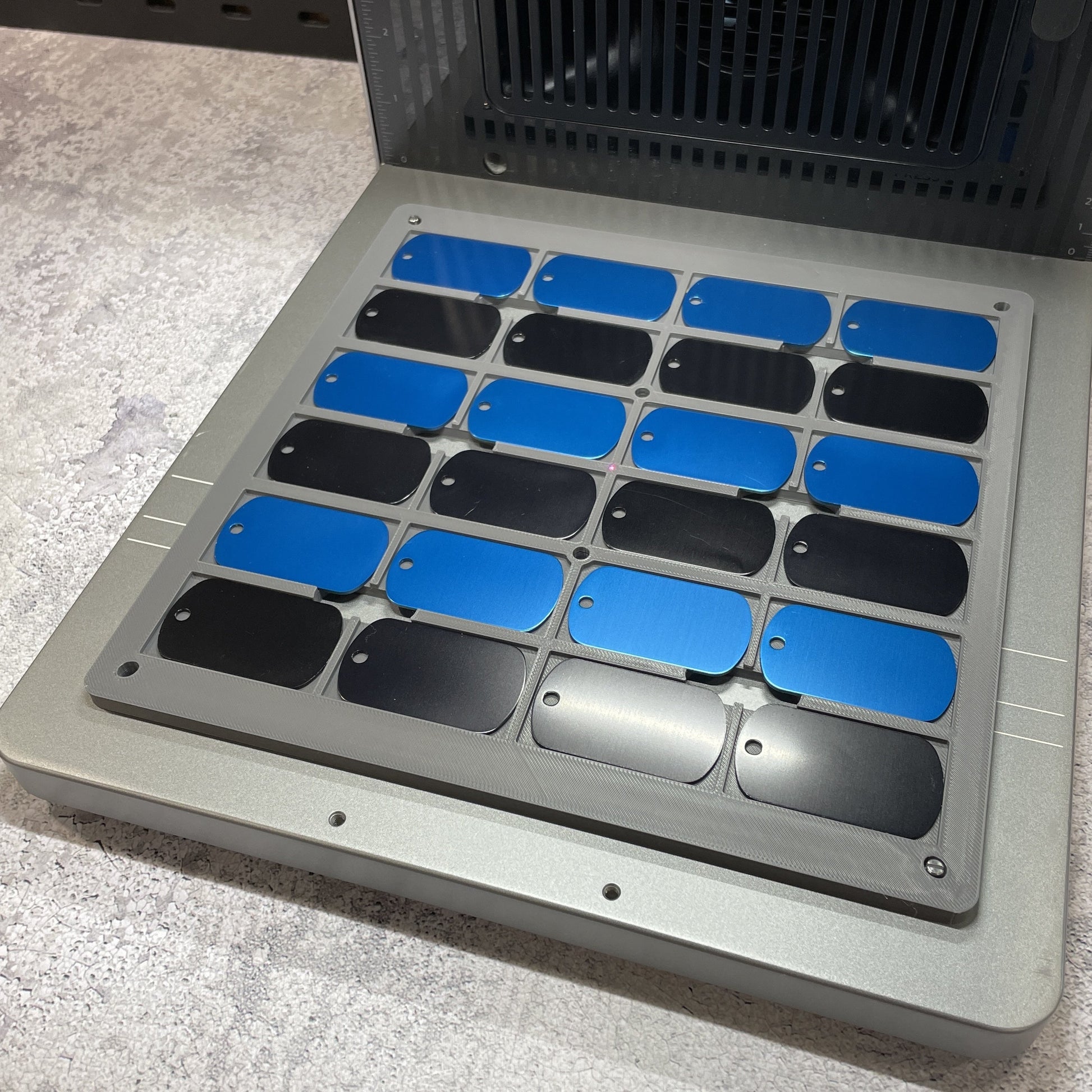 Samcraft military dog tag jig on the xTool F2 Ultra bed, holding a full grid of blue and black dog tags.