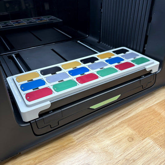 Samcraft military dog tag jig on the bed of an xTool Omni UV printer, holding eighteen anodized aluminum tags in gold, black, silver, blue, red and green.
