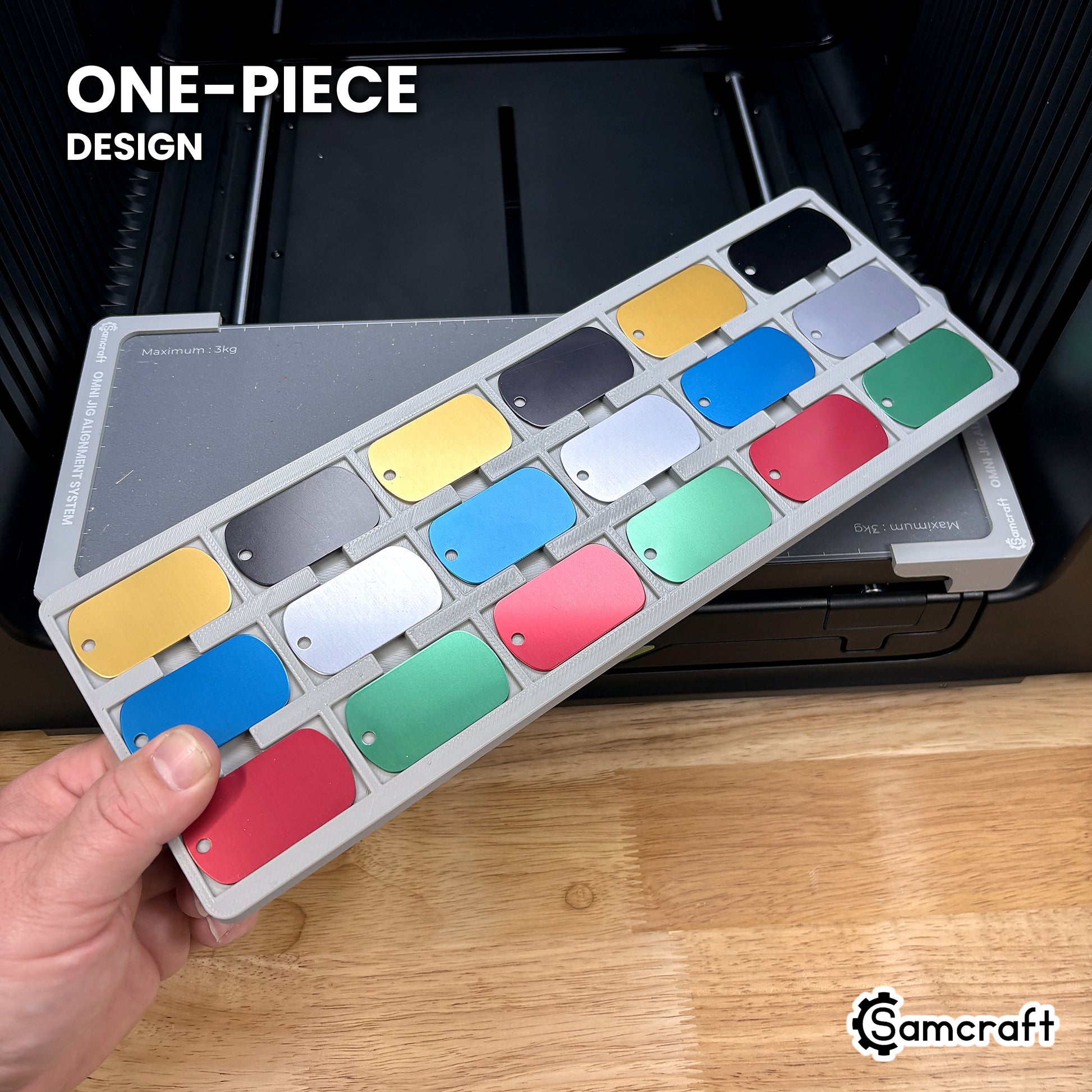 Hand holding the one-piece Samcraft military dog tag jig for the xTool Omni, a single molded gray tray filled with eighteen anodized tags.