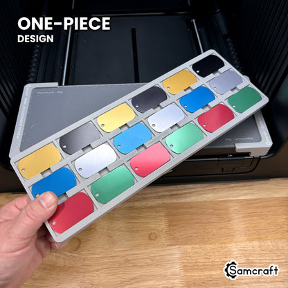 Hand holding the one-piece Samcraft military dog tag jig for the xTool Omni, a single molded gray tray filled with eighteen anodized tags.