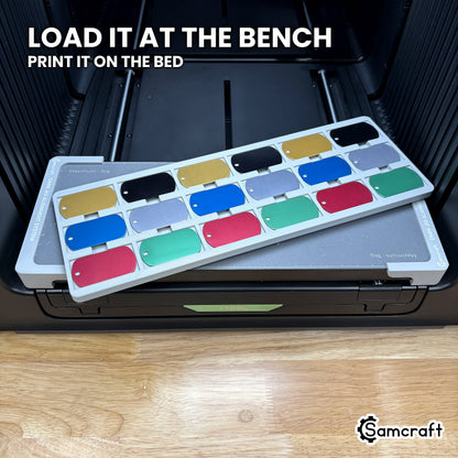 The loaded Samcraft military dog tag jig lifted at an angle above the xTool Omni bed, showing it can be filled away from the machine and set down to print.