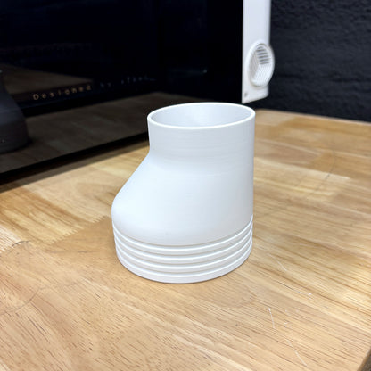 White Samcraft offset 4 inch exhaust hose adapter for the xTool Omni standing on a wood bench in front of the printer, showing the grooved 4 inch end and the smaller port end.