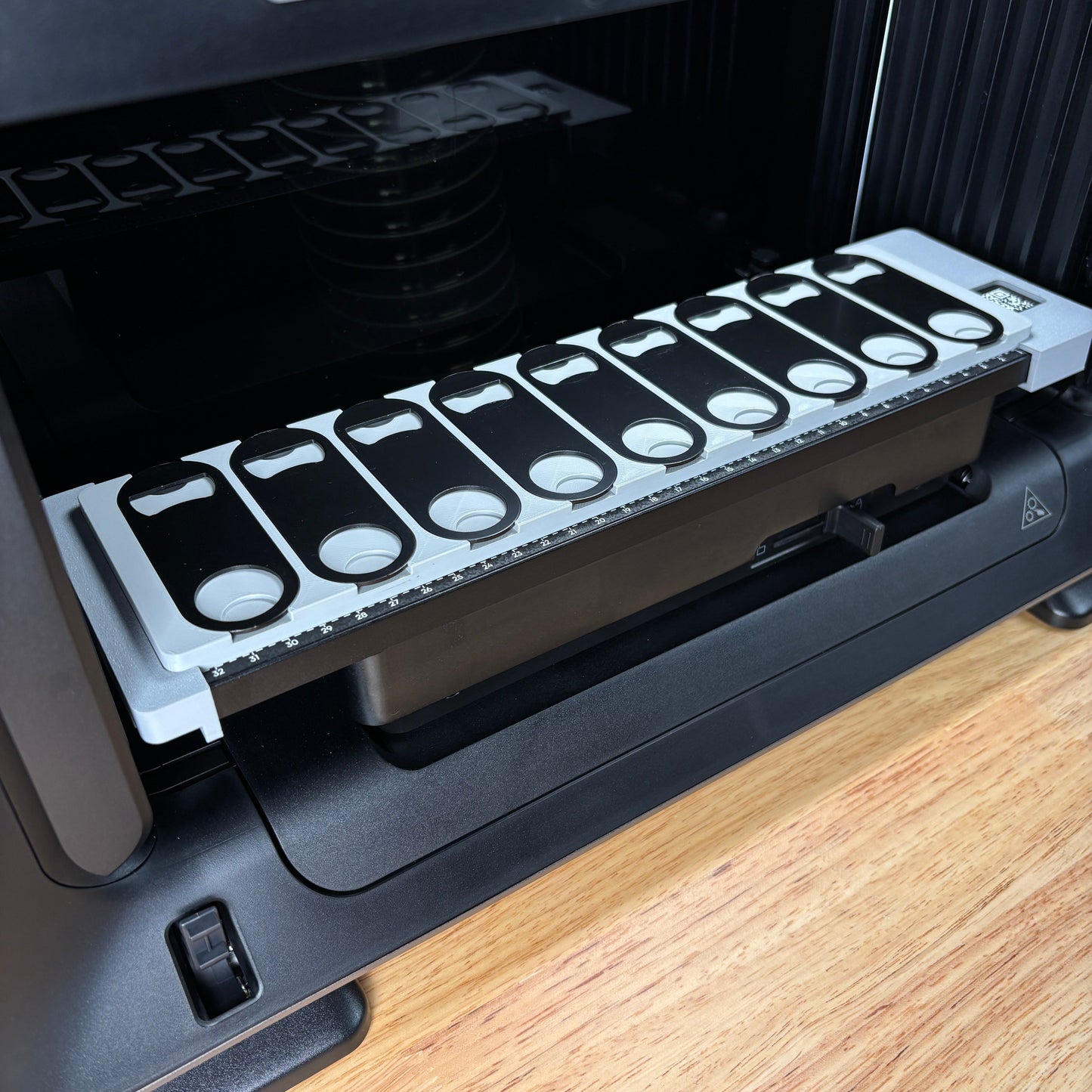 Samcraft oval bottle opener jig on the eufyMake E1 print bed, holding a row of flat black oval metal bottle openers.