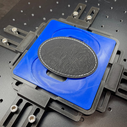 Samcraft blue oval patch jig on a ComMarker laser bed, holding a dark oval leatherette patch.
