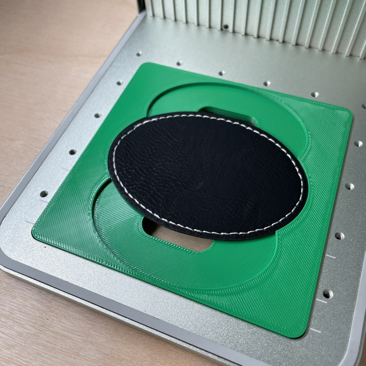 Samcraft oval patch jig in an xTool F1 laser bed, holding a large black leatherette oval patch.