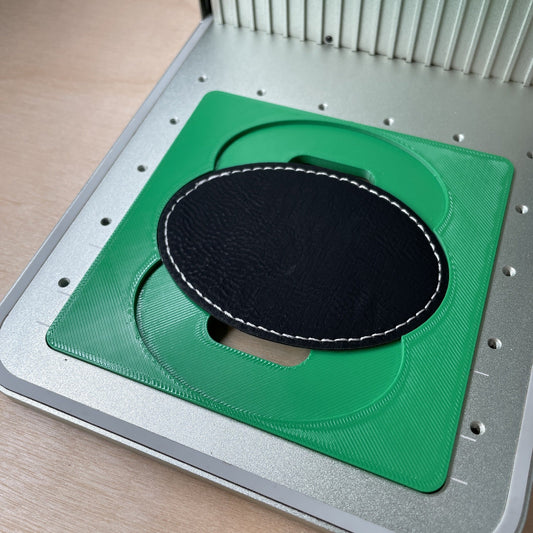 Samcraft oval patch jig in an xTool F1 laser bed, holding a large black leatherette oval patch.