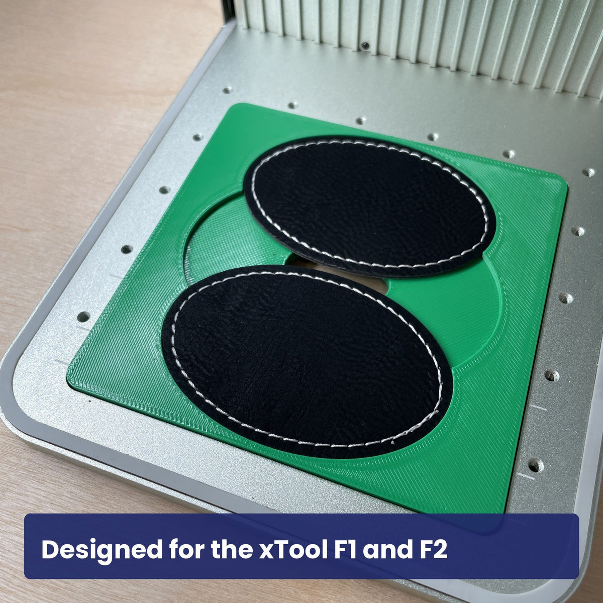 Samcraft oval patch jig in the xTool F1 base plate holding two black leatherette oval patches.