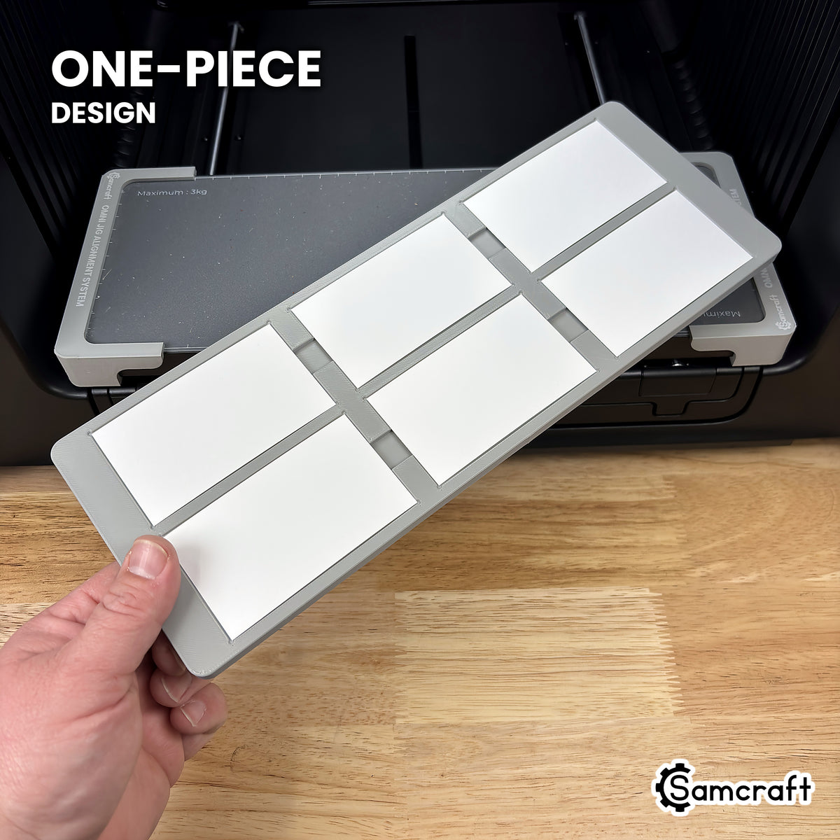 Hand holding the one-piece Samcraft paper business card jig for the xTool Omni, loaded with six business cards, in front of the printer bed.