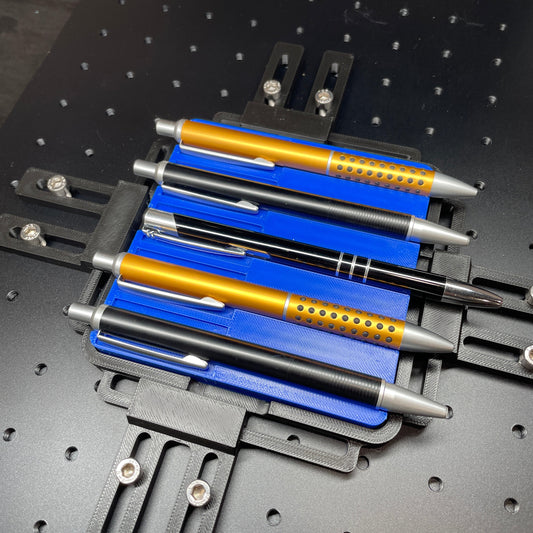 Samcraft blue pen jig on a ComMarker laser bed, holding gold and blue metal pens.