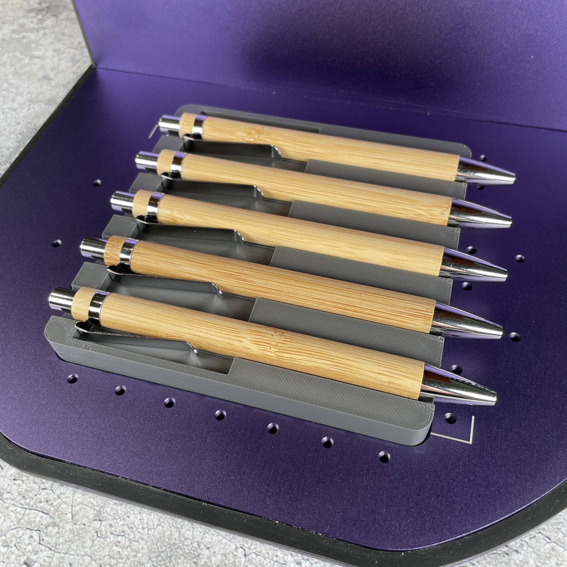 Samcraft universal pen jig on the purple bed of a WeCreat Lumos, holding a row of bamboo pens.