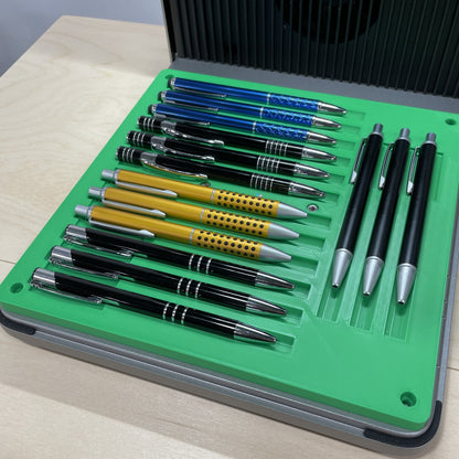 Samcraft green universal pen jig in an xTool F1 Ultra laser bed, holding a row of metal pens in gold, blue and black.