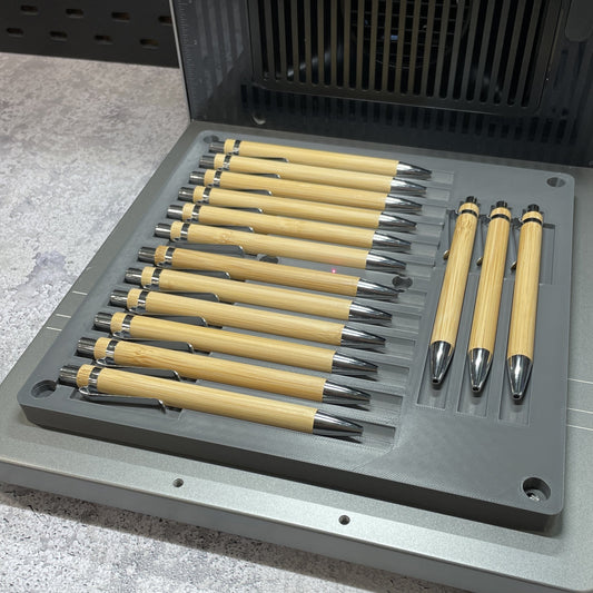 Samcraft universal pen jig on the xTool F2 Ultra bed, holding bamboo and black metal pens side by side.