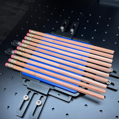 Samcraft blue hexagon pencil jig on a ComMarker laser bed, holding a row of wooden pencils.