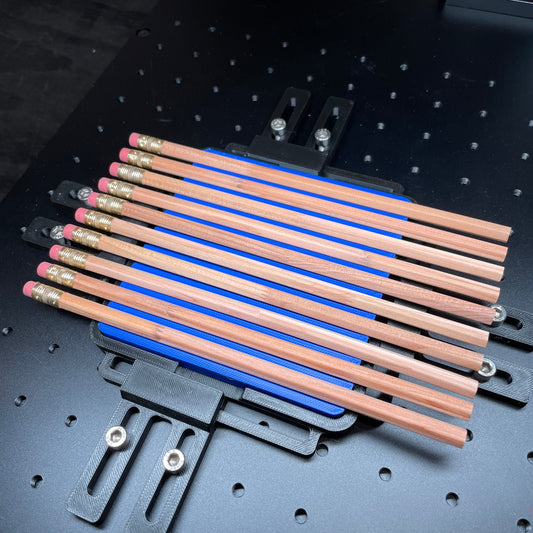 Samcraft blue hexagon pencil jig on a ComMarker laser bed, holding a row of wooden pencils.