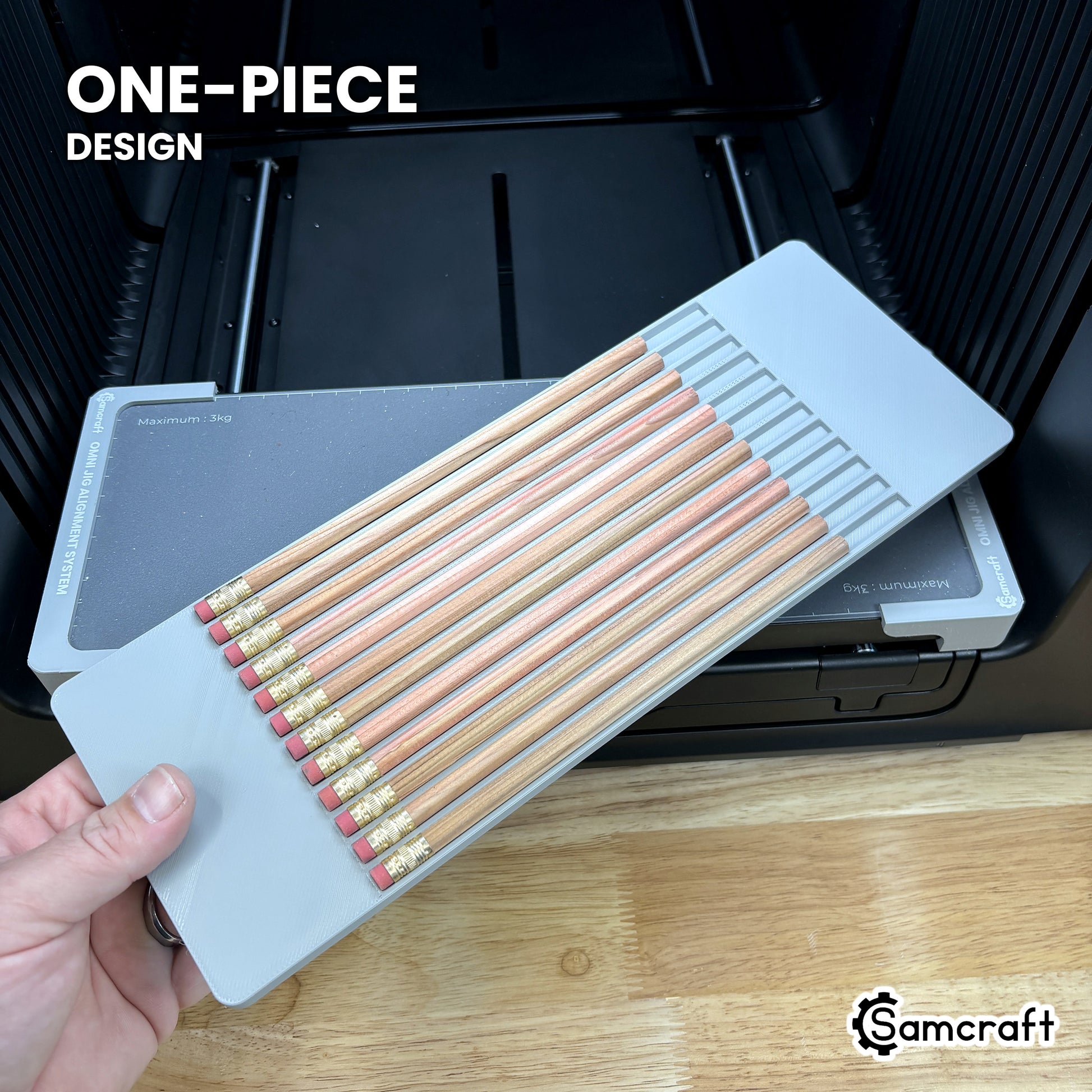 Hand holding the one-piece Samcraft hexagon pencil jig for the xTool Omni, a single molded gray tray loaded with twelve pencils.