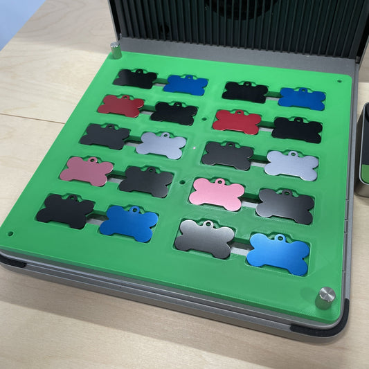 Samcraft green bone pet tag jig in an xTool F1 Ultra laser bed, holding bone-shaped aluminium pet tags in several colours.