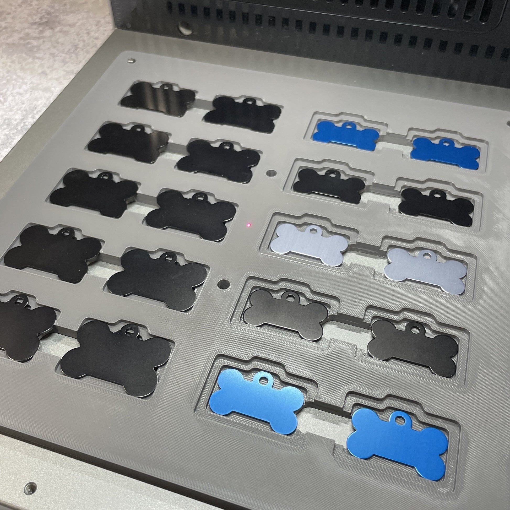 Samcraft bone pet tag jig on the xTool F2 Ultra bed, holding bone-shaped pet tags in black, silver and blue.