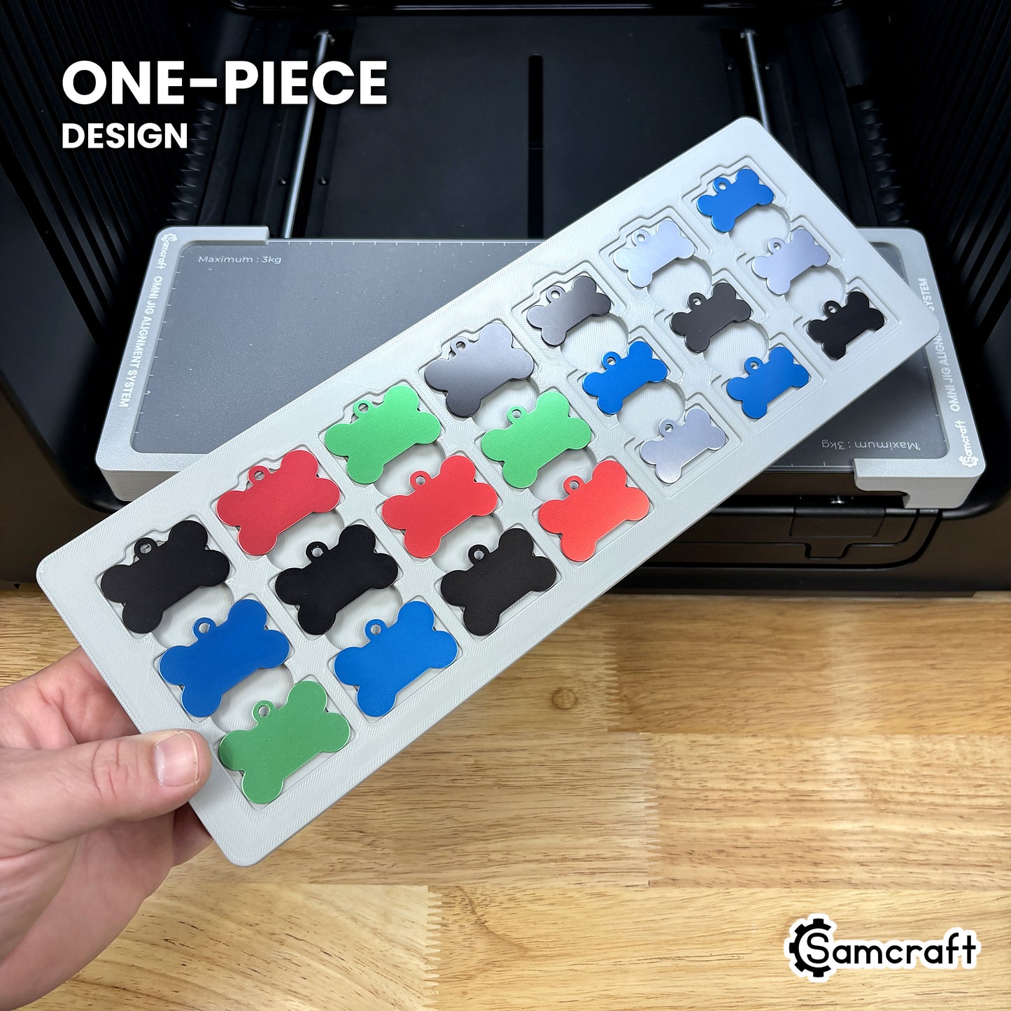 Hand holding the one-piece Samcraft bone pet tag jig for the xTool Omni, 21 colored aluminum bone tags seated in a single molded gray tray.