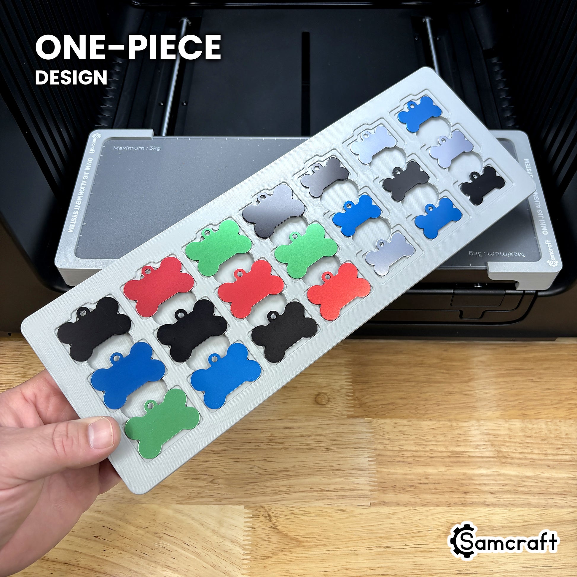 Hand holding the one-piece Samcraft bone pet tag jig for the xTool Omni, 21 colored aluminum bone tags seated in a single molded gray tray.