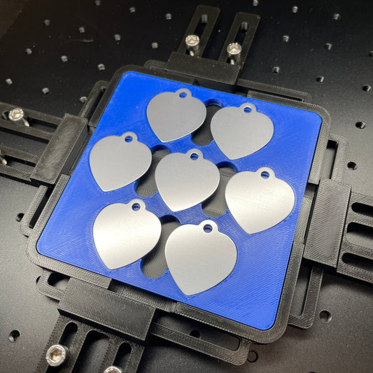 Samcraft blue heart pet tag jig on a ComMarker laser bed, holding a set of stainless pet tags.