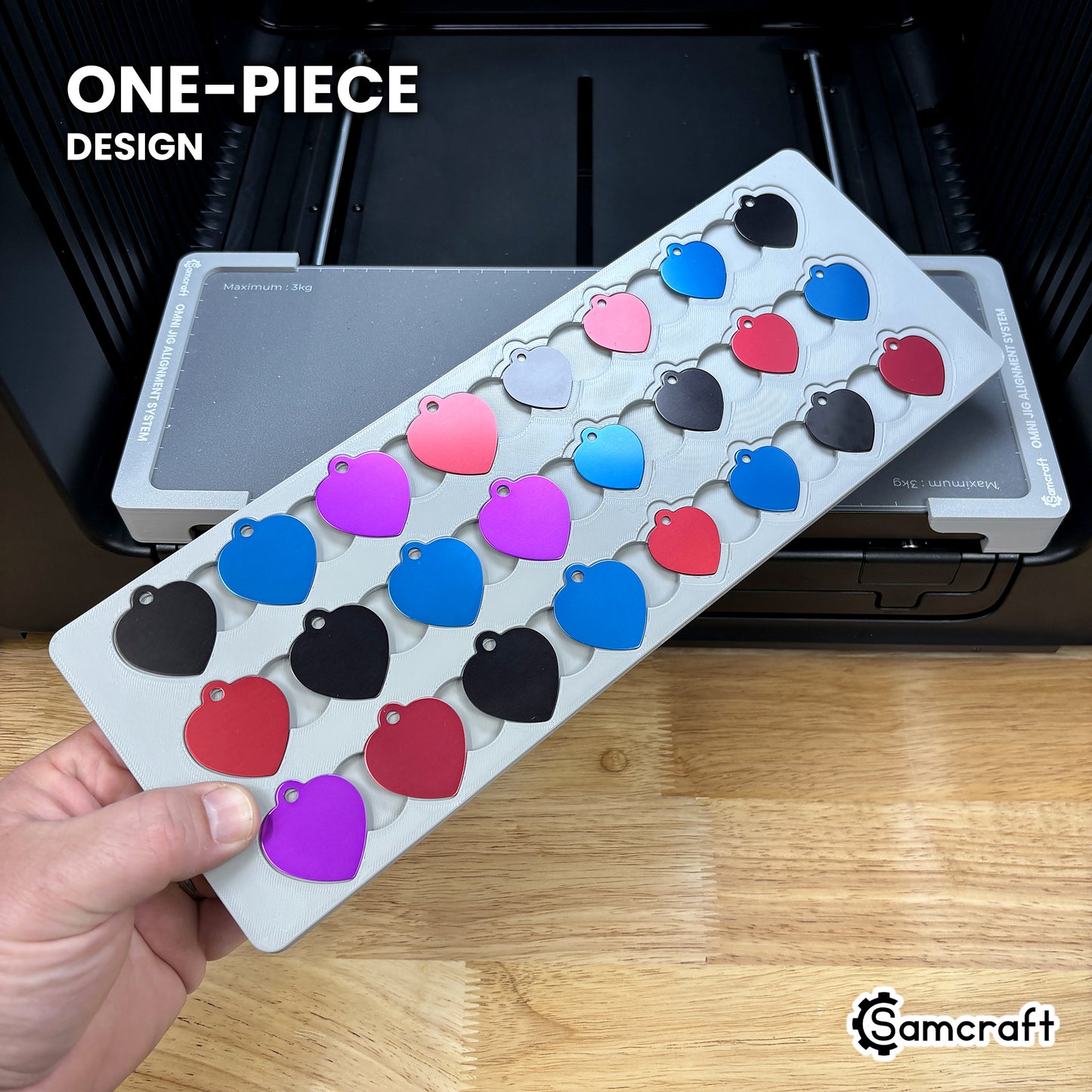 Hand holding the one-piece Samcraft heart pet tag jig for the xTool Omni, colored aluminum heart tags seated in a single molded gray tray.