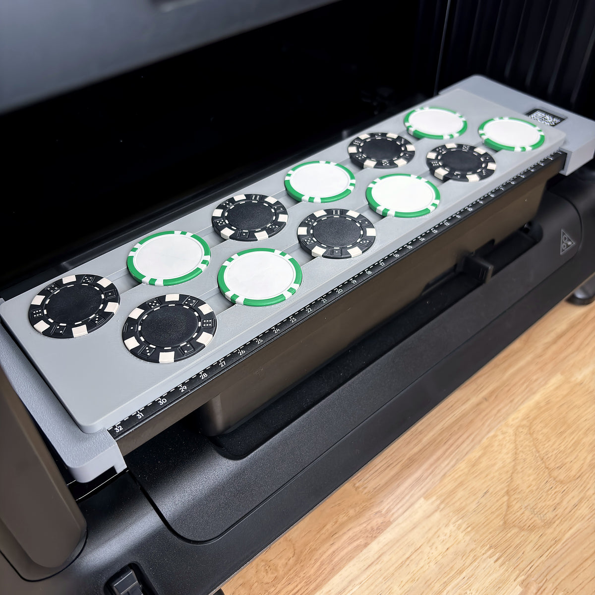 Samcraft poker chip jig on the bed of a eufyMake E1 UV printer, loaded with 12 poker chips in two staggered rows, black dice-stripe chips alternating with white chips edged in green stripes.